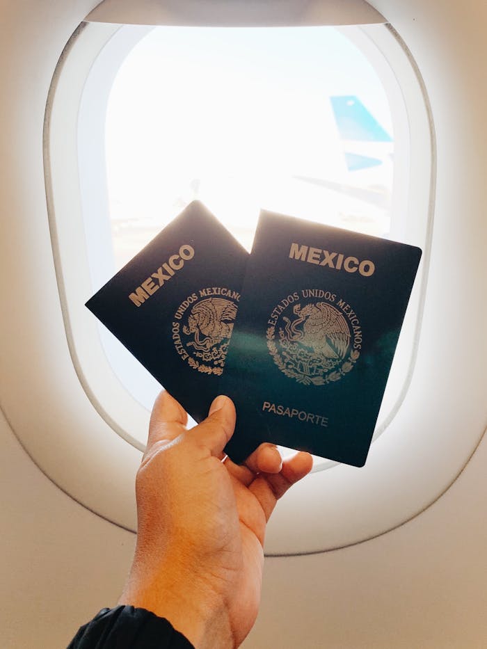 A hand holding two Mexican passports near an airplane window.